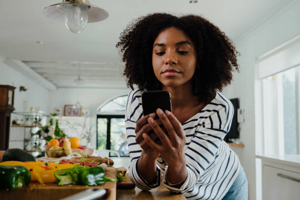 istockphoto-1278556226-612×612 Beautiful focussed African American female researching lunch recipe on smartphone standing next to chopped vegetables in organised kitchen. High quality photo